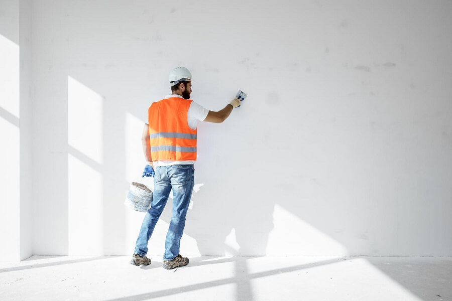Un ouvrier qui tient une boîte de peinture et peint le mur en blanc