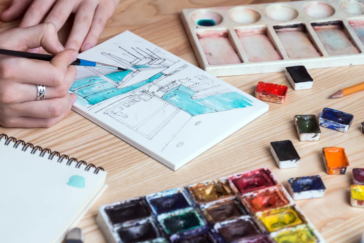 Une personne qui dessin une cuisine sur une feuille avec plusieurs palettes de couleurs sur la table