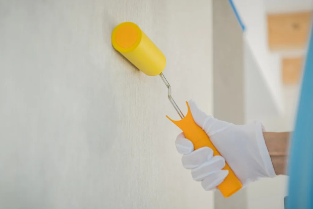 Une personne avec un rouleau jaune et blanc qui travaille sur un mur