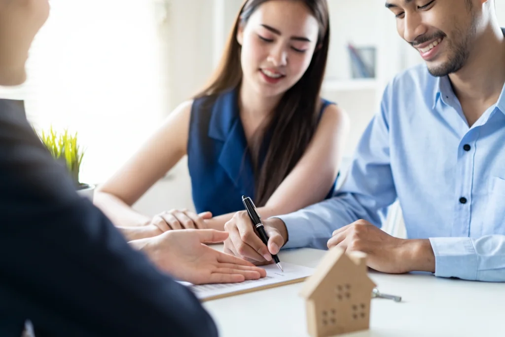 Un couple en train de signé des documents sur une table à côté d'une maquette de maison
