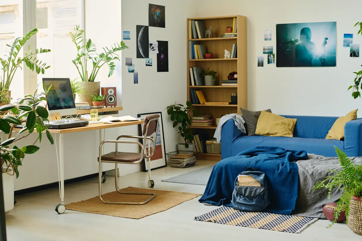 Un espace avec un étagère dans un angle et un table de bureau sur un autre angle ainsi qu'un canapé bleu 