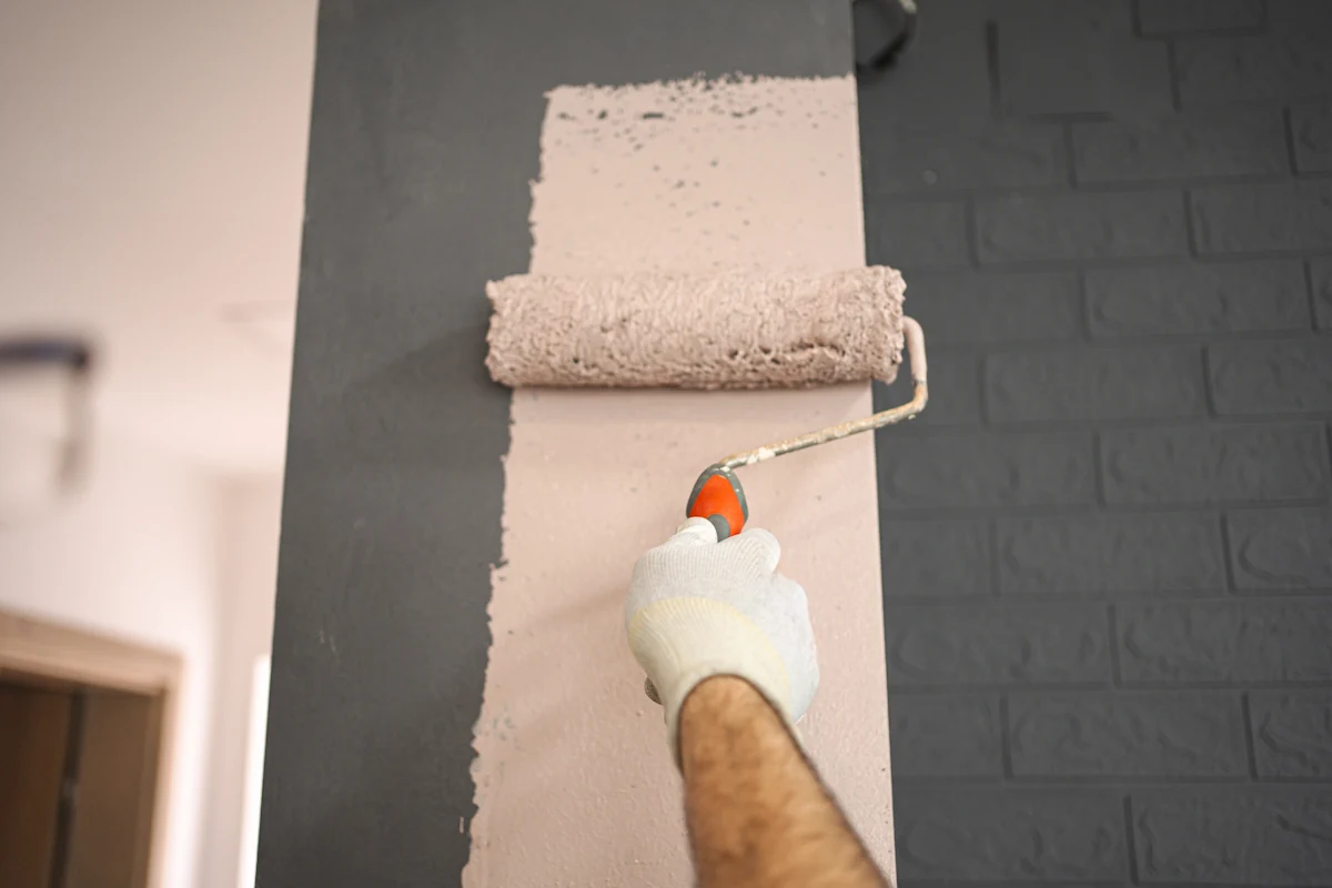Une personne qui applique une couleur rose sur un mur en brique gris avec un rouleau
