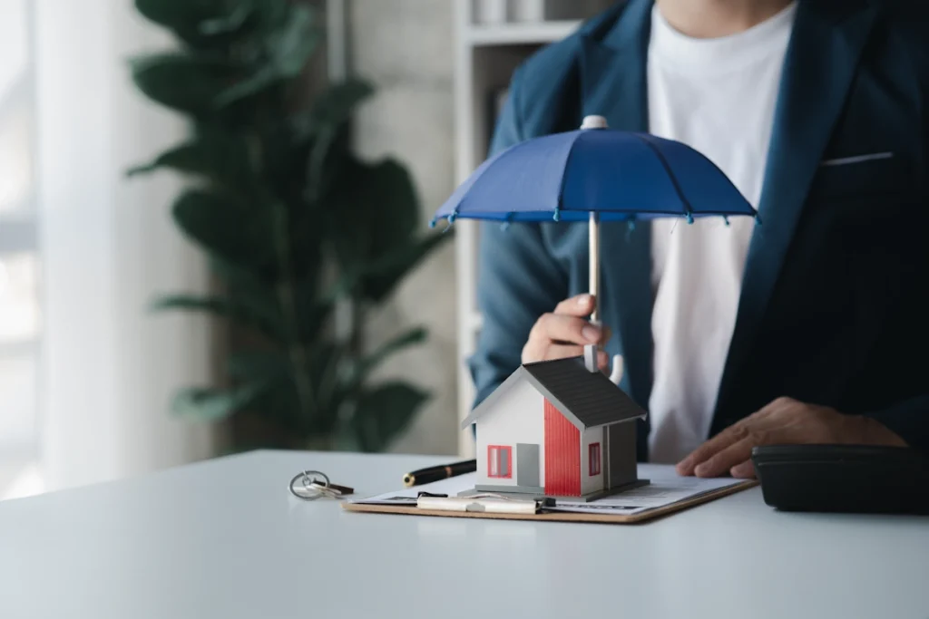 un homme qui tient un parapluie bleu en dessus d'une maquette de maison posée sur une table