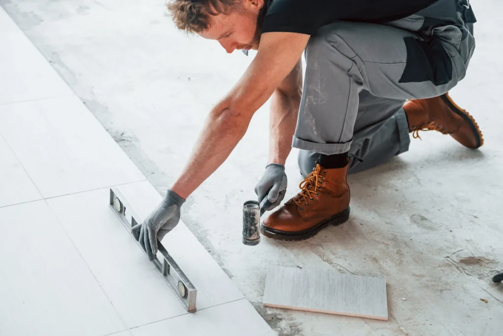 Un homme qui pose un carreau avec n marteau et un vérificateur de niveau