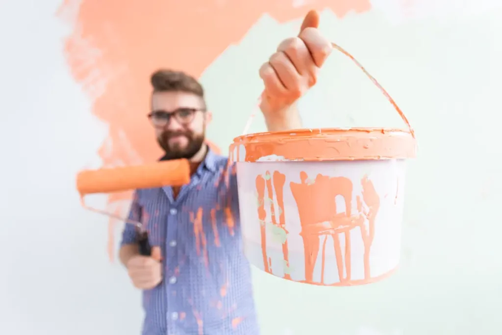 Un homme qui tient un pot de peinture orange dans une main et un rouleau dans l'autre
