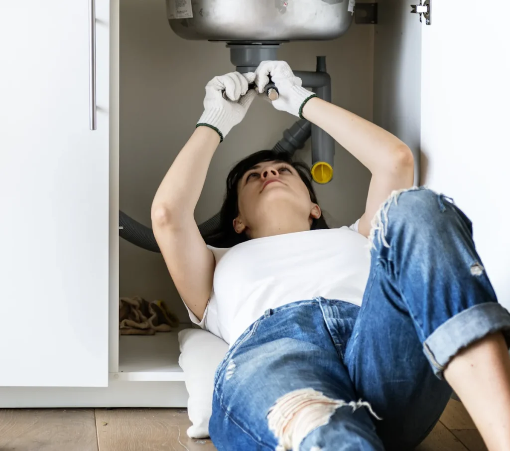Une femme sous un évier qui répare une fuite d'eau