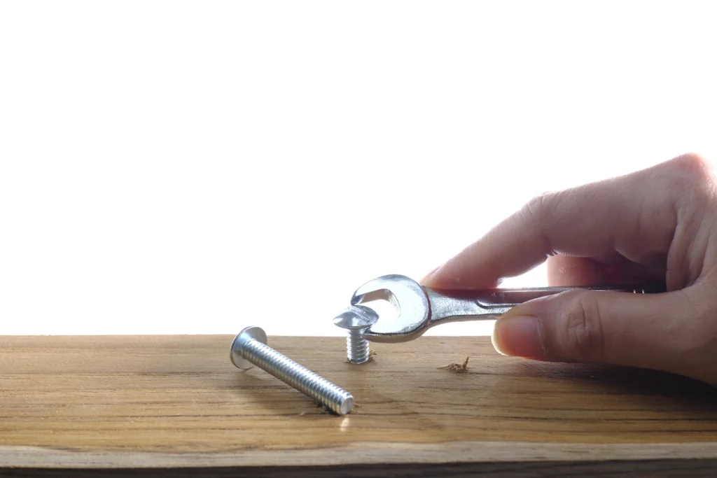 Une personne qui essaie d'enlever un vis dans du bois avec une clé
