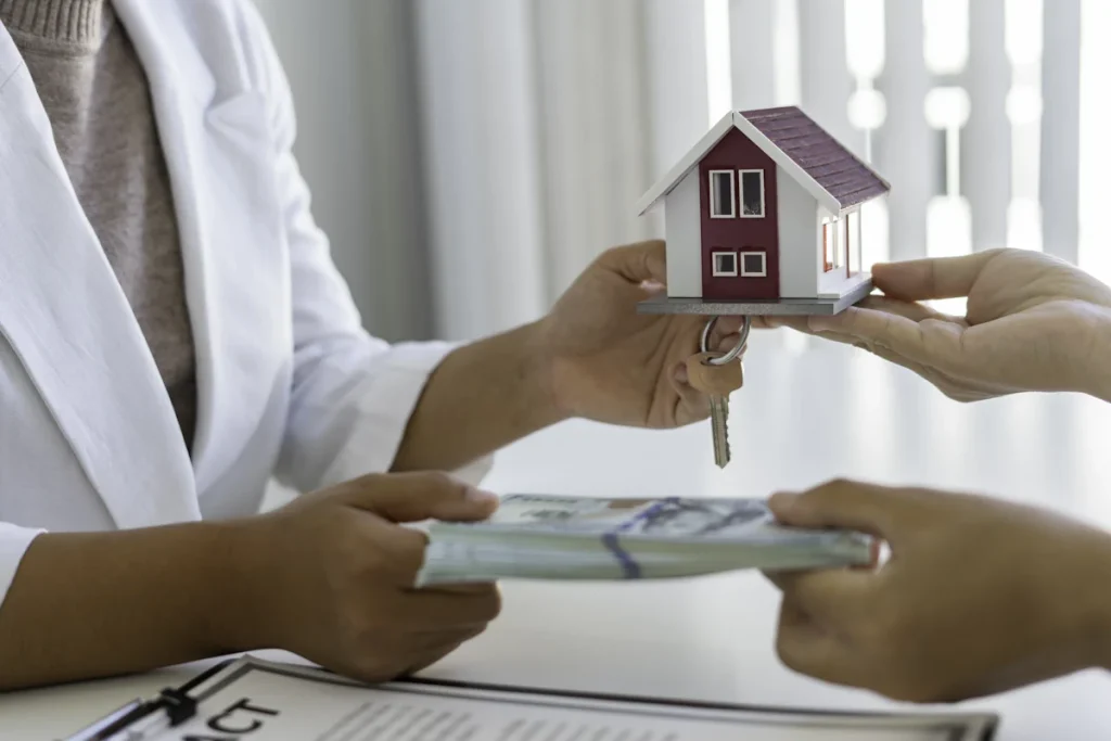 Une personne qui tend de l'argent à une autre et récupère une maquette de maison et des clés