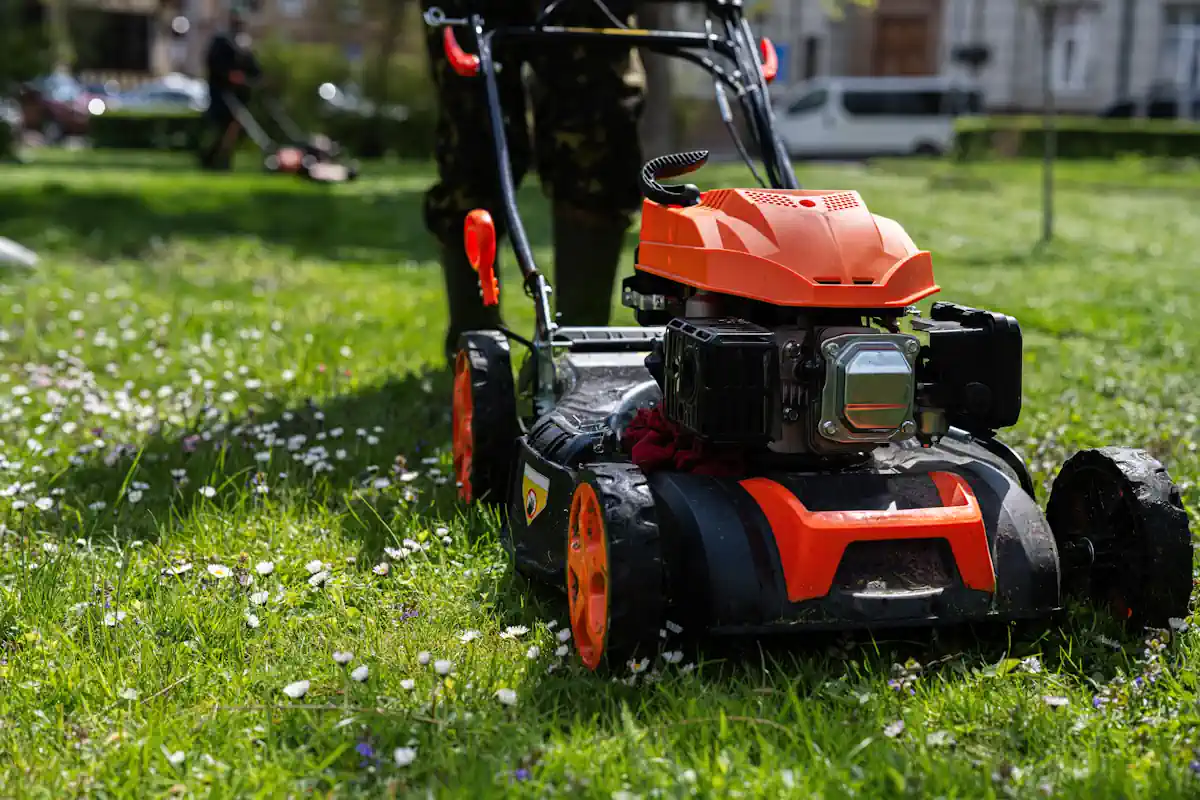 Un homme avec une tondeuse thermique qui entretien un jardin