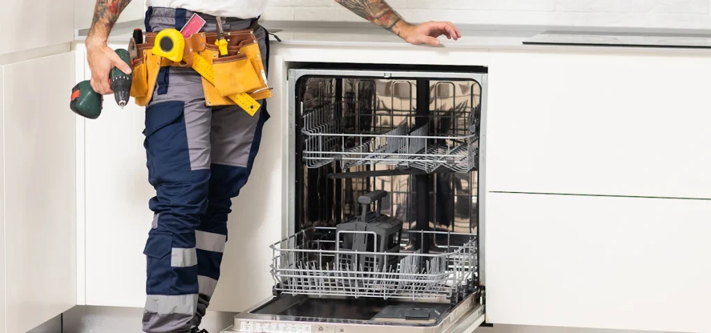Un homme avec des outils de bricolage qui regarde un lave-vaisselle ouvert vide