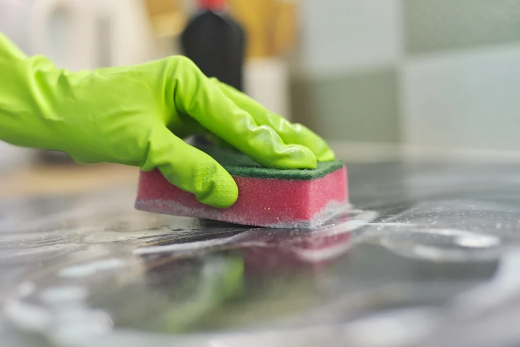 Une personne qui porte un gant vert et nettoie un plan de travail de cuisine avec une éponge