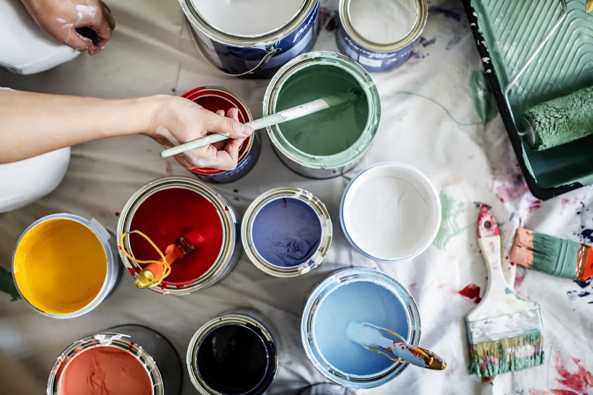 Différents pots de peinture posés sur le sol devant une personne qui fait des tests avec un pinceau
