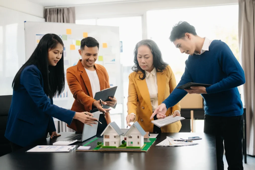 Un groupe de personne qui discute autour d'une maquette de maison psoée sur la table