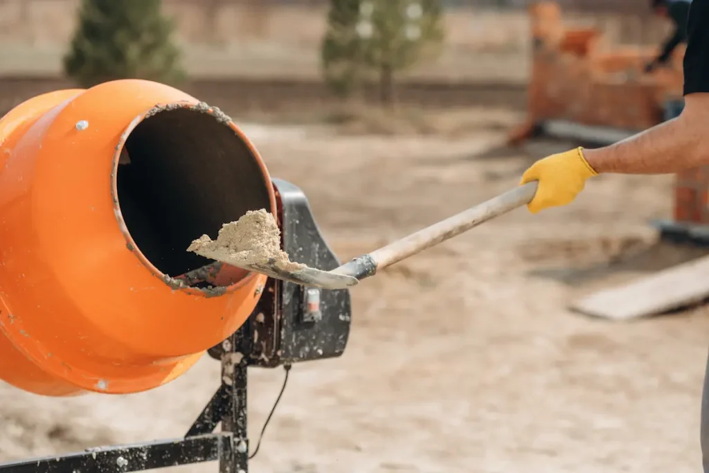 Une personne qui verse du mortier dans une bétonnière avec une pelle