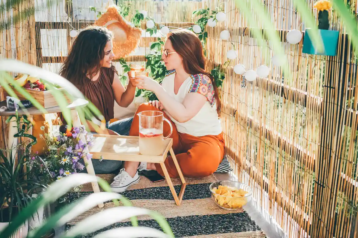 deux femmes assises sur le sol sur un balcon bordé de canisses