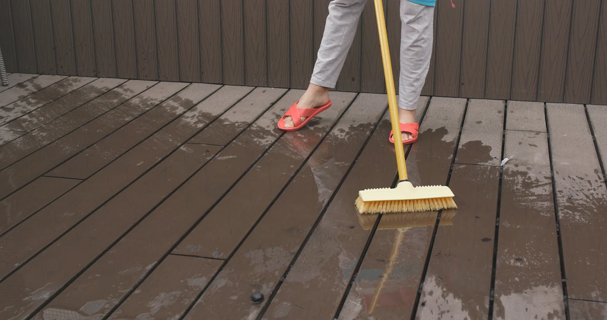 Une personne qui nettoie une terrasse avec une balai brosse dur