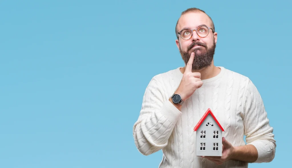 un homme pensif qui tient une maquette de maison enbois