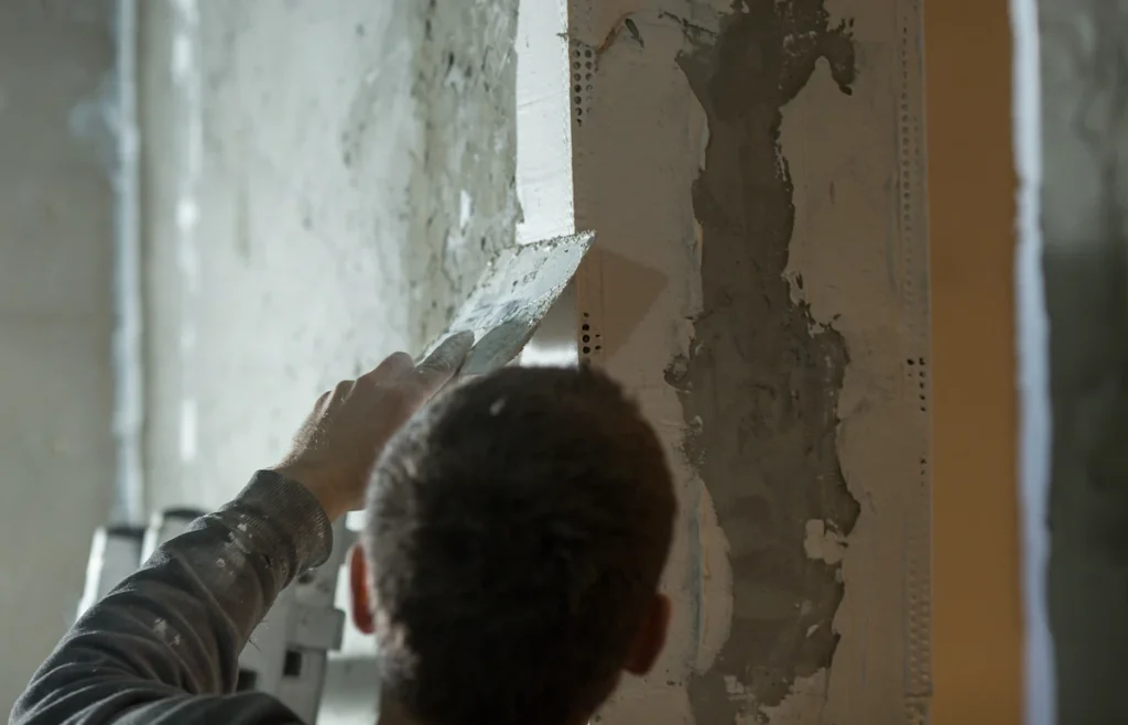 Un homme qui rebouche un trou sur un mur en friable